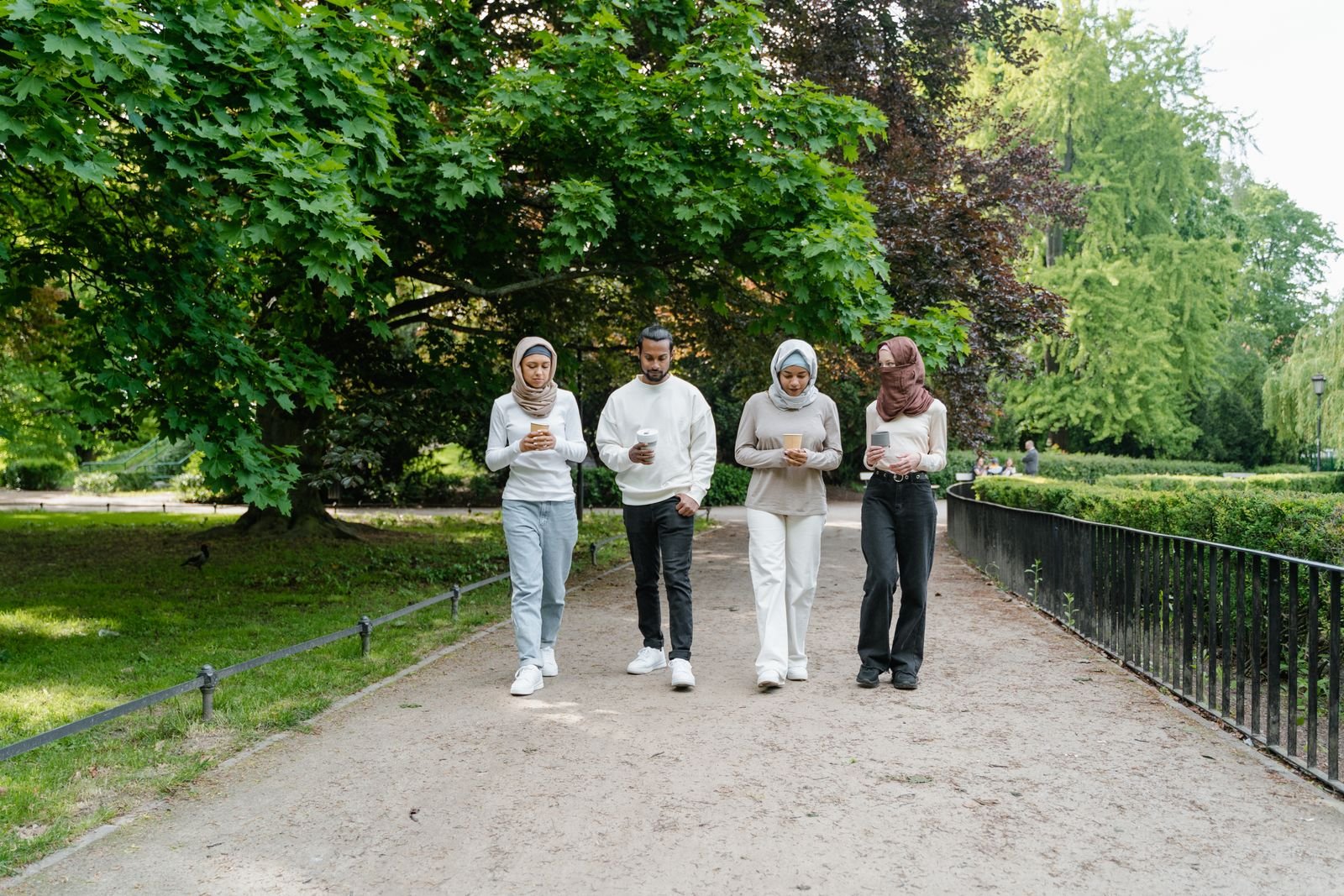 A small group of friends walking together along a tree-lined park path on a sunny day